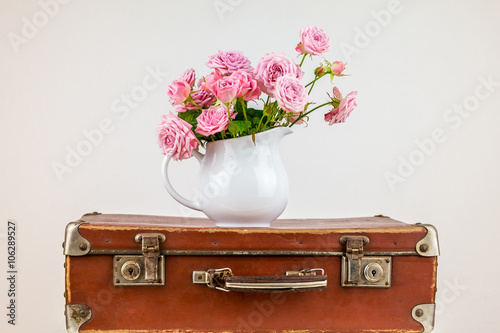 Flowers in jug on old brown vintage suitcase.