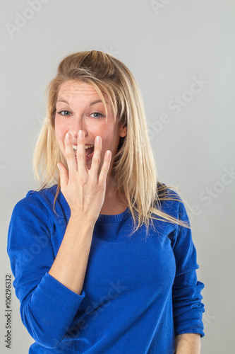 successful smile - adorable young blond woman laughing with hand hiding her mouth for fun and joy, grey background studio