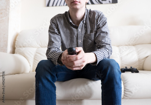 Young man sitting on couch and holding remote controller in hand