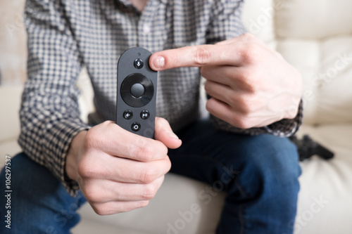 Young man sitting on couch and holding remote controller in hand