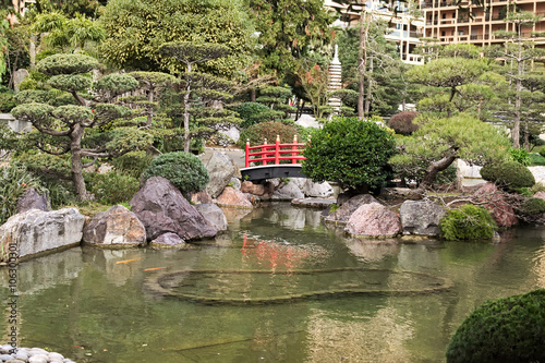 Japanese Garden in Monaco in the early morning. Part of the red bridge is hidden behind a bush
