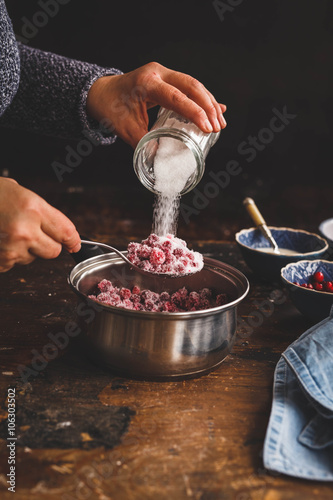 Red berries jam. Person making jam, jelly, confiture over rustic wooden table.