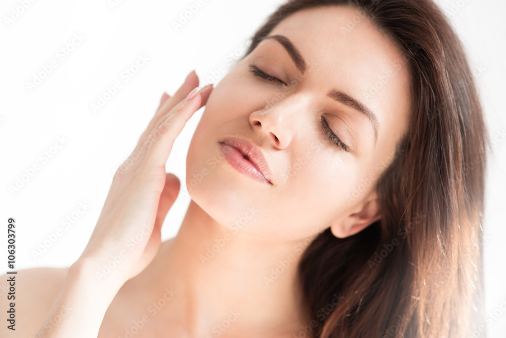 Close up portrait of beautiful woman with healthy skin on white background with closed eyes and hand on her face