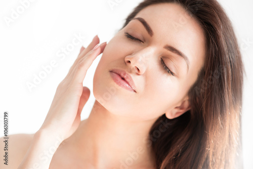 Close up portrait of beautiful woman with healthy skin on white background with closed eyes and hand on her face