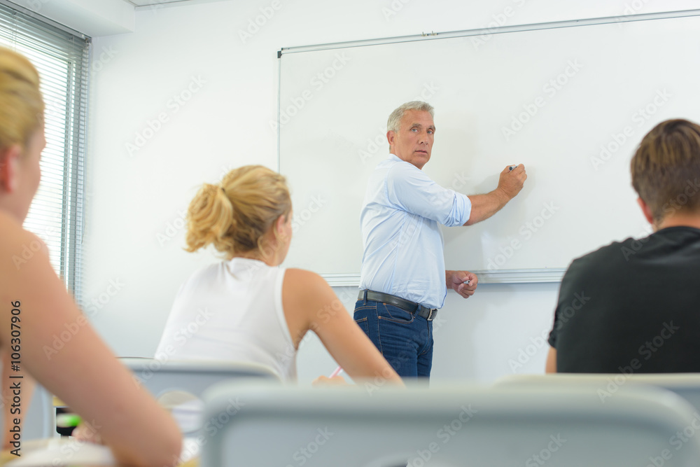 Teacher writing on whiteboard in front of class Teacher writing on whiteboard in front of class