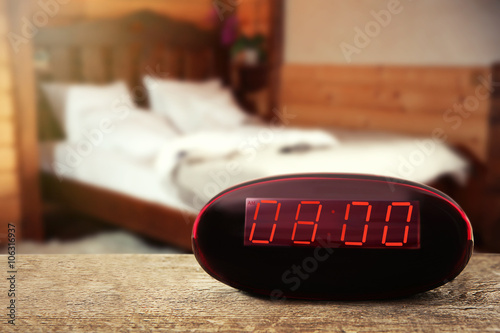 Digital clock showing 8:00 o'clock on wooden table, bedroom background