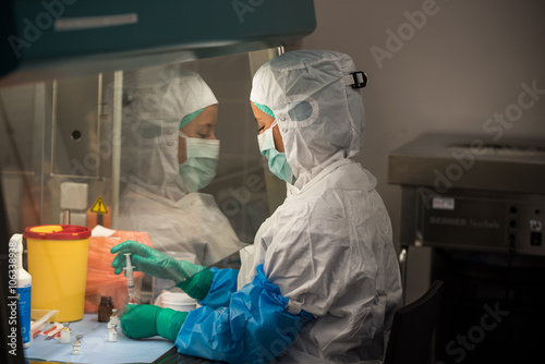 Junge hochkonzentrierte pharmazeutisch technische Assistentin PTA bereitet sterile Arzneimittel unter dem Abzug im Laminar-Airflow zu photo