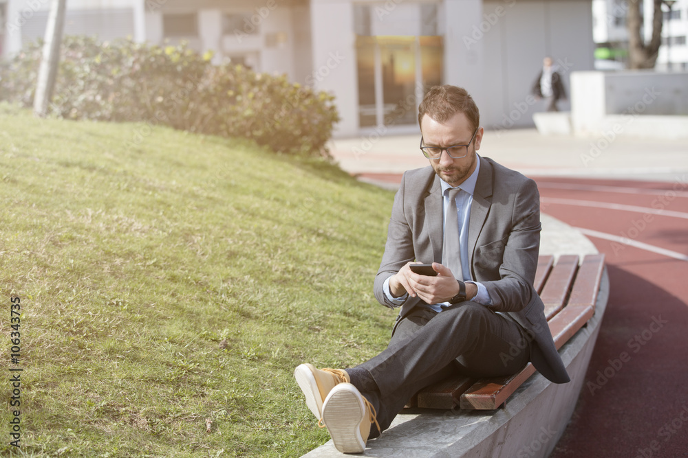 Fototapeta premium Businessman using his smart phone while resting on the bench 
