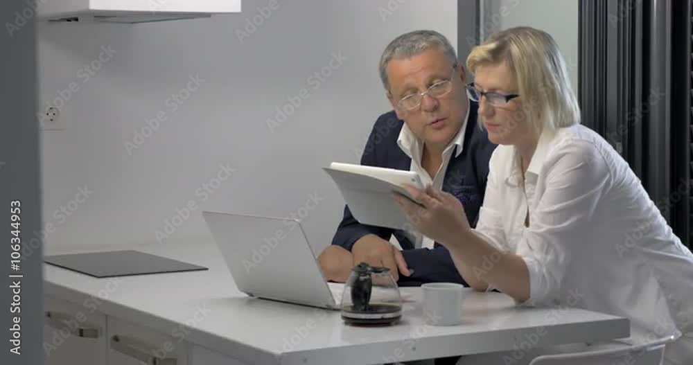 Couple of adults looking at tablet and talking in kitchen Couple of adults looking at tablet and talking in kitchen