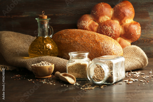 Composition of seeds in banks, bread, buns and oil on wooden table background, closeup