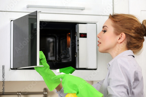 Young woman cleaning microwave with a sponge