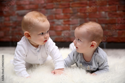 Two adorable babes playing in the room against brick wall background photo