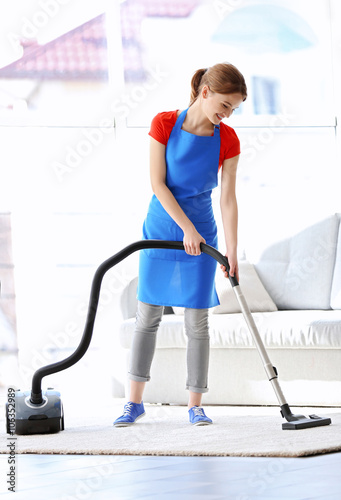Cleaning concept. Young woman cleaning carpet with vacuum cleaner