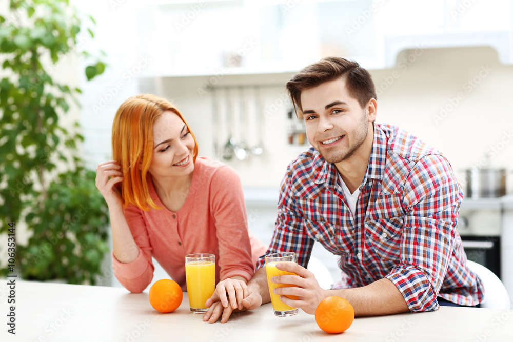 Young beautiful couple with glasses of orange juice in the kitchen