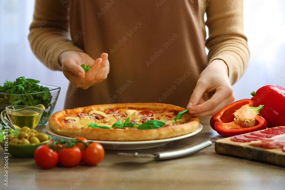 Woman decorating fresh baked pizza with basil, close up