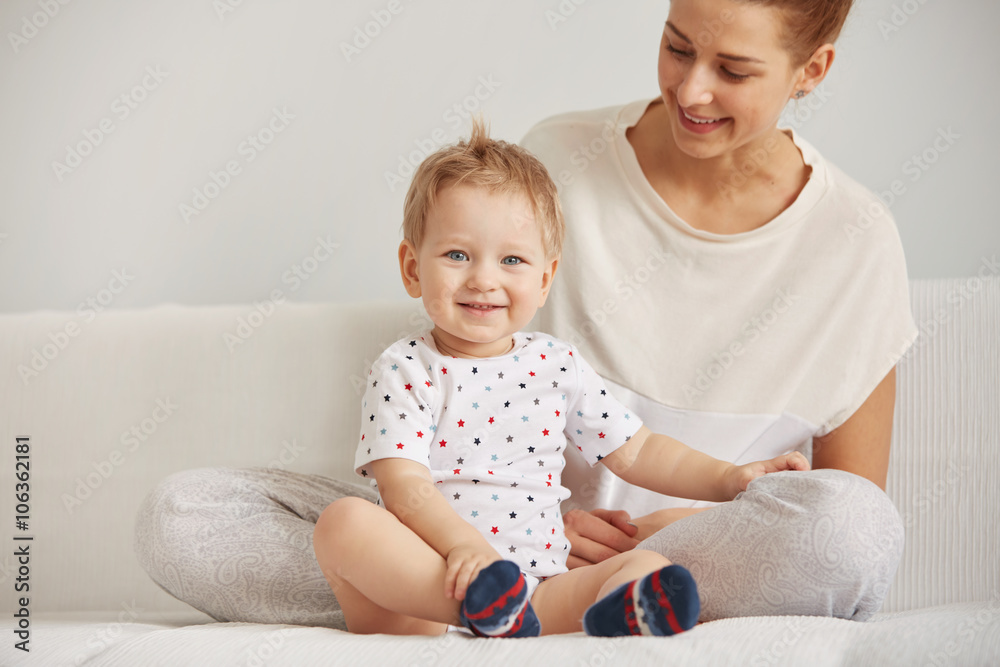 Young mother with her one years old little son dressed in pajamas are relaxing and playing in the bedroom at the weekend together, lazy morning, warm and cozy scene. Selective focus. Young mother with her one years old little son dressed in pajamas are relaxing and playing in the bedroom at the weekend together, lazy morning, warm and cozy scene. Selective focus.