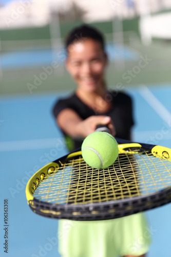 Tennis player woman showing ball on racquet / tennis racket. Unrecognizable female athlete holding fitness equipment - closeup of yellow ball on outdoor summer court. Sport activity.