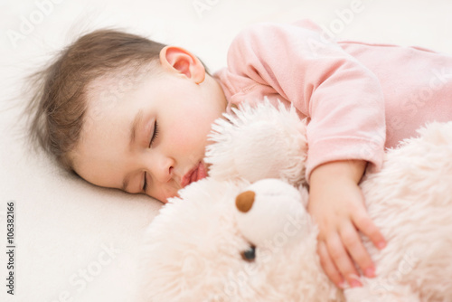 Close-up portrait of beautiful baby toddler girl sleeping with a fluffy teddy bear on the bed