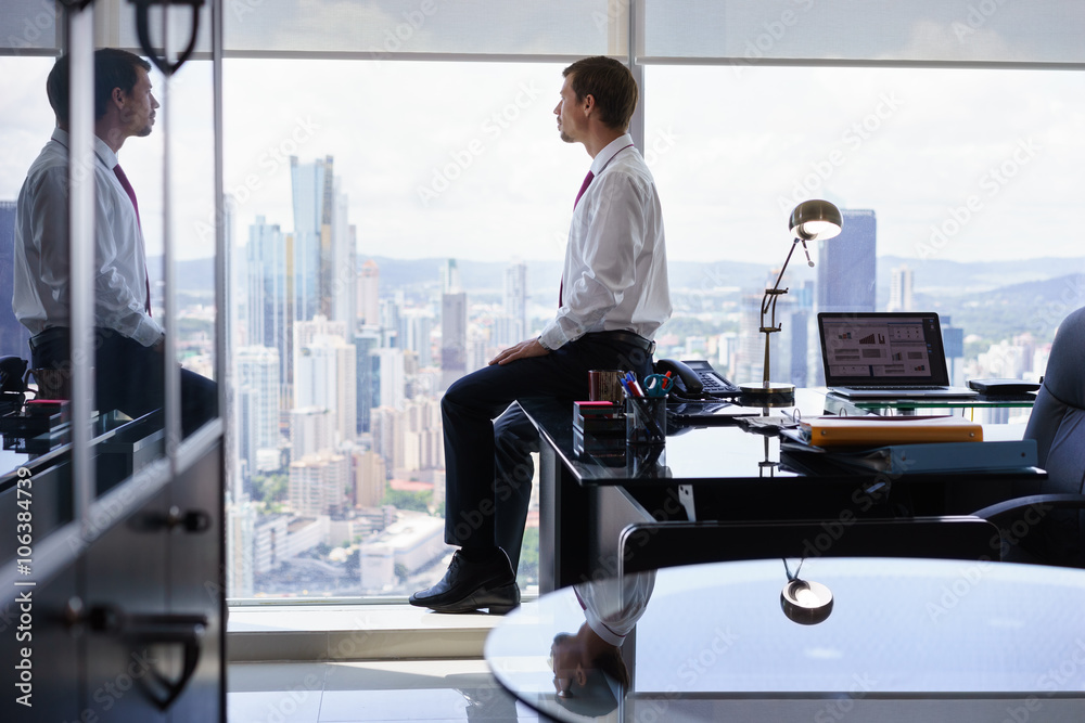 Business Person Sits On Desk Looking Out Of Office Window Business Person Sits On Desk Looking Out Of Office Window