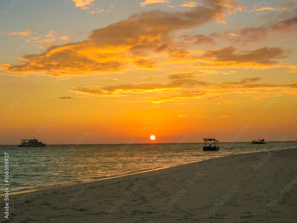 Maldives background. Sunset over the tropical sea and coral beach with colorful clouds in the sky. Boats on the horizon in heavenly atoll of peace and relaxation. North Male Atoll Asdu, Indian Ocean.