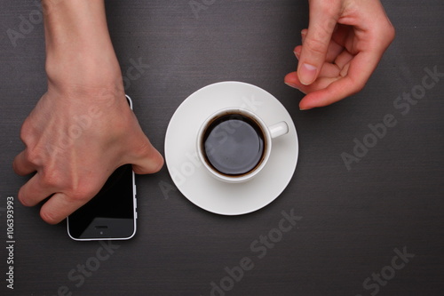 Woman hands touching smart phone and holding coffee cup. Top view