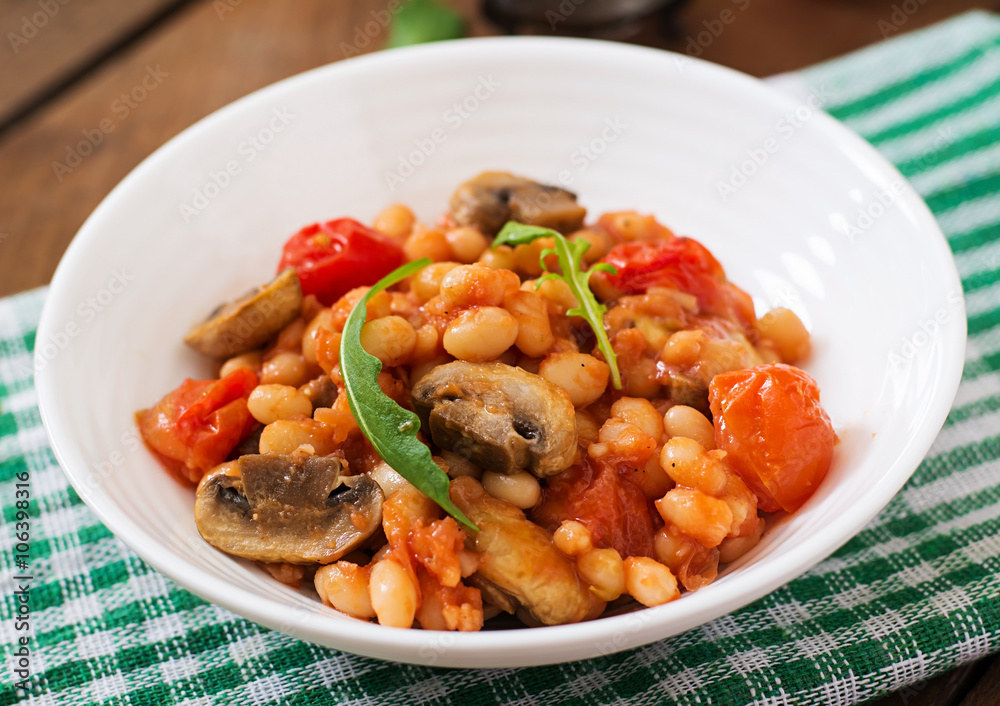 Stewed white beans with mushrooms and tomatoes with spicy sauce in a white bowl