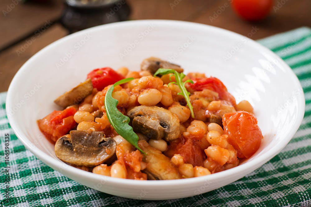 Stewed white beans with mushrooms and tomatoes with spicy sauce in a white bowl