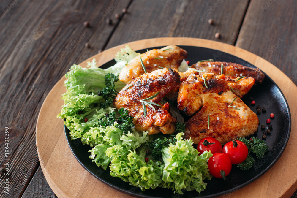 Grilled chicken wings with fresh vegetables. Baked chicken meat with lettuce and tomatoes cherry. Homemade meat on wooden table. 