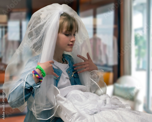 Teen girl trying on wedding dress and veil. The concept of early marriage, dreams of a wedding.  photo