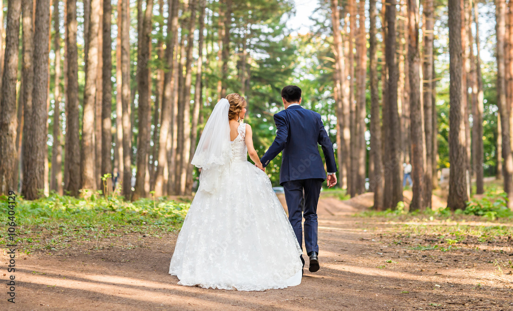 Bride and groom walking away in summer park outdoors