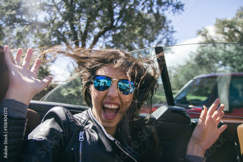 Woman with sunglasses and hands up in a convertible car