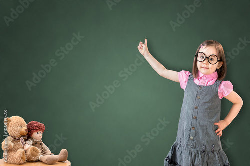 Cute little girl wearing business dress and show something on green chalk board.