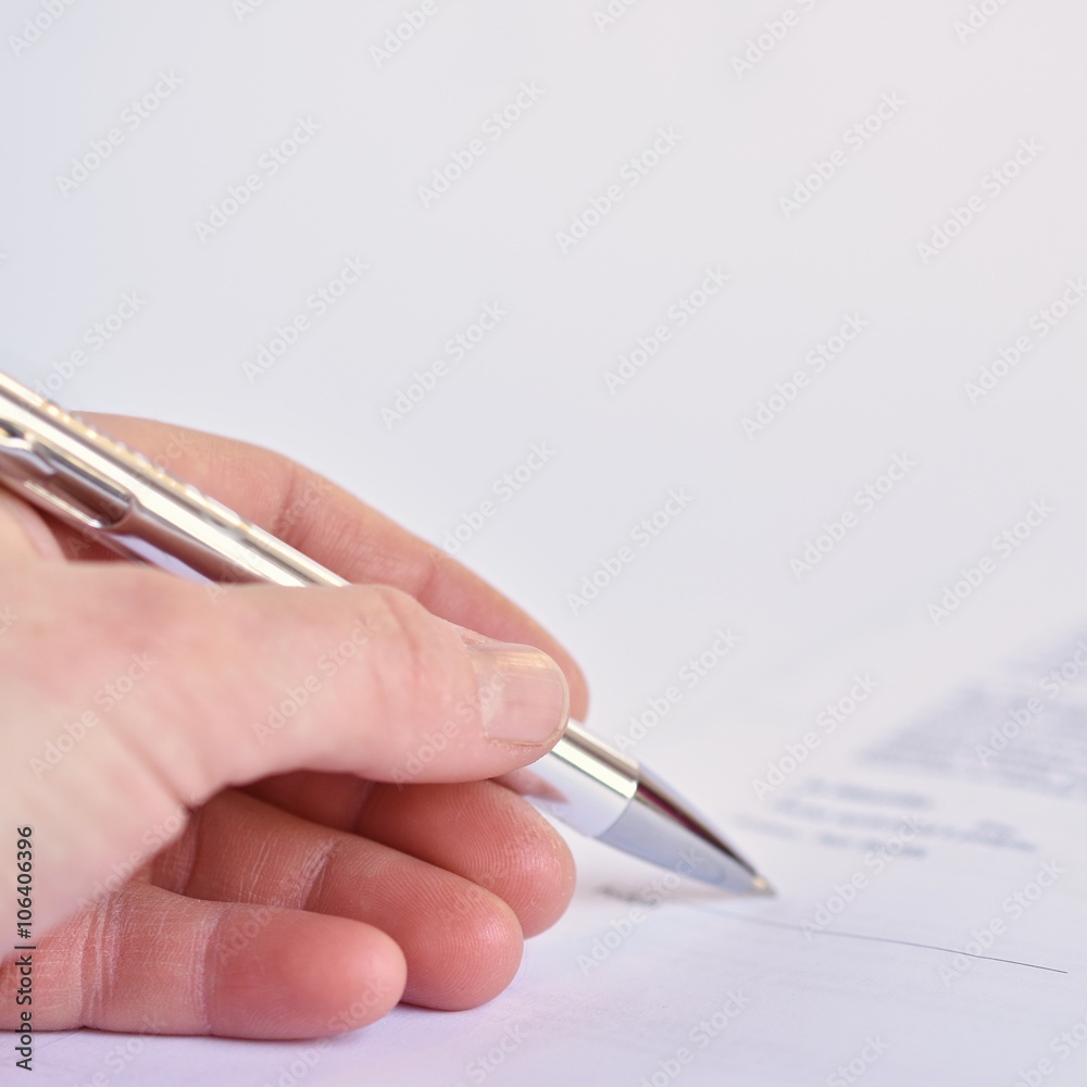Hand with a pen when signing a document on paper. Hand with a pen when signing a document on paper.