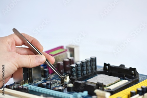 Hand with tweezers above board with components. Repair of computers and modern technologies.