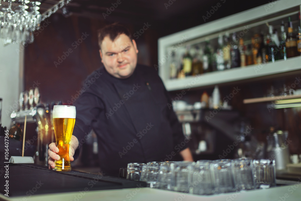Pouring fresh beer. Close-up of young bartender pouring beer while standing at the bar counter.
