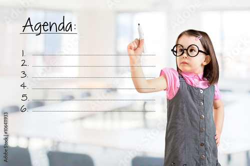 Cute little girl wearing business dress and writing blank agenda list. Office background.