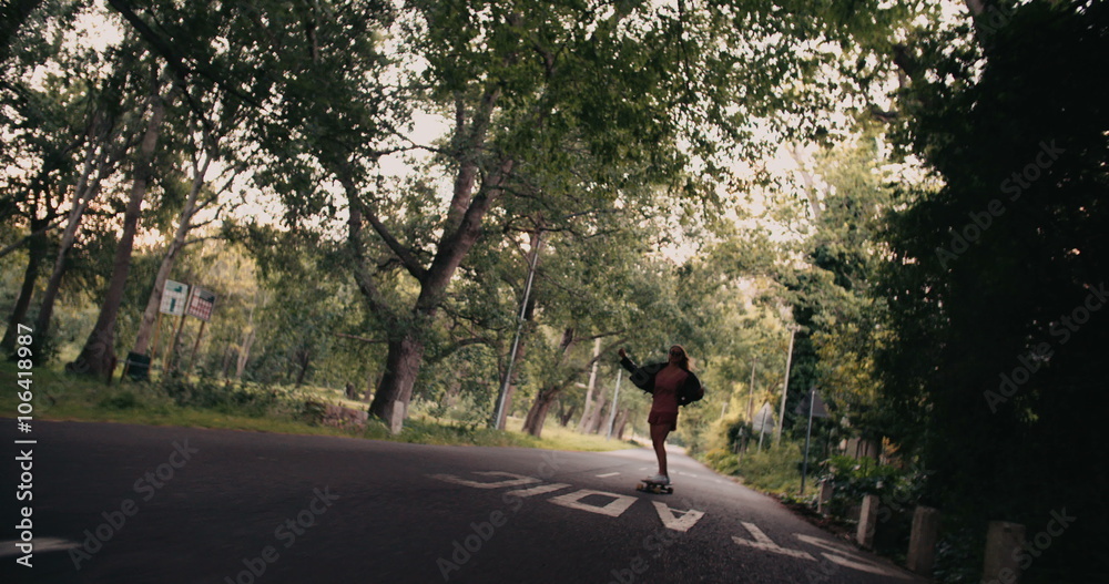 Teenage girl riding her longboard along a tree-lined road Teenage girl riding her longboard along a tree-lined road