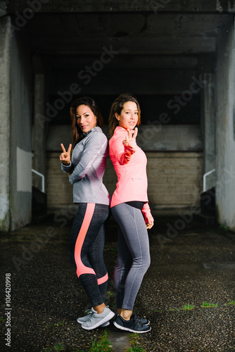 Two successful fitness women doing victory and success gesture after urban workout. Female athletes standing under the rain outside. © Dirima