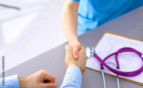 Attractive female doctor shaking a patient's hands in her office