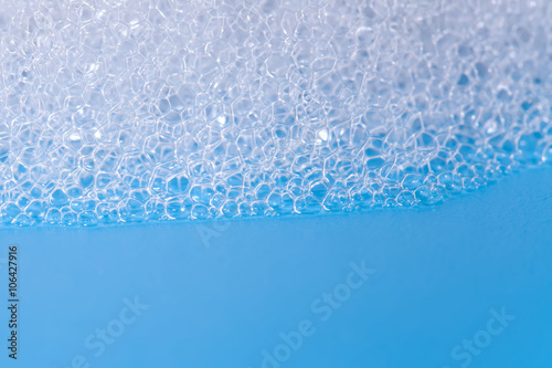 Soap bath bubbles macro view. Laundry detergent, suds textured pattern. White soapsuds on blue background, copy text, horizontal photo.