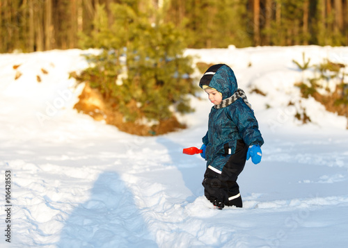 Little boy with toy scoop looking at shadow on snow
