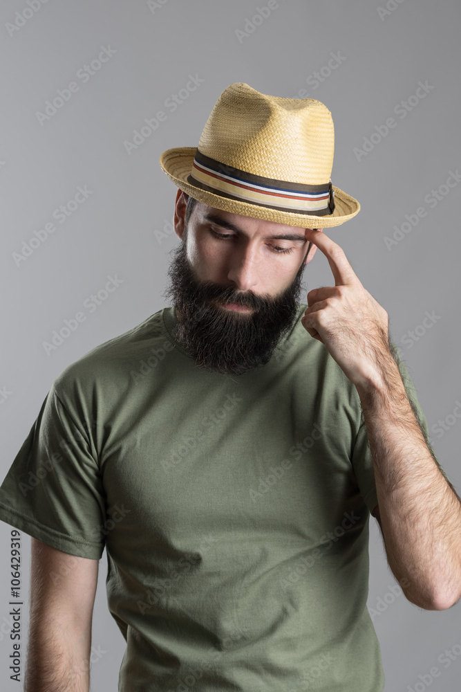 Worried thinking bearded man wearing straw hat looking down and scratching hand with finger. Portrait over gray studio background. Worried thinking bearded man wearing straw hat looking down and scratching hand with finger. Portrait over gray studio background.