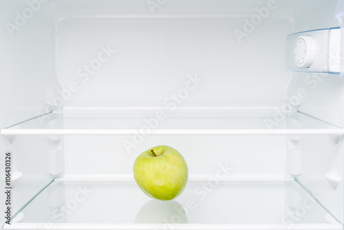 Green apple in empty refrigerator. Diet and hunger concept
