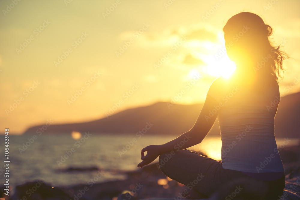 woman meditating in lotus pose on the beach at sunset