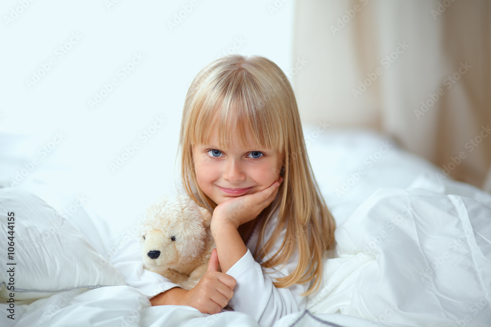 Little girl with teddy bear lying on the bed at home