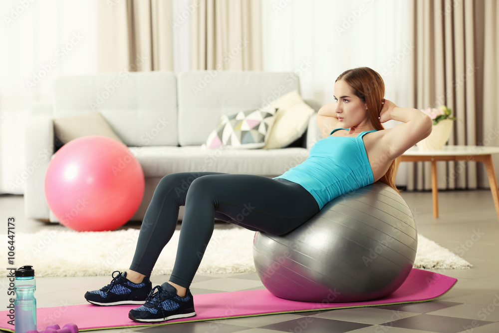 Fototapeta premium Young sportswoman doing exercises with ball on a mat at home