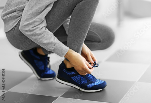 Woman tying shoelaces of sneaker on a floor