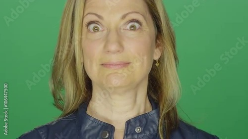 Beautiful middle aged woman making funny faces, on a green screen studio background