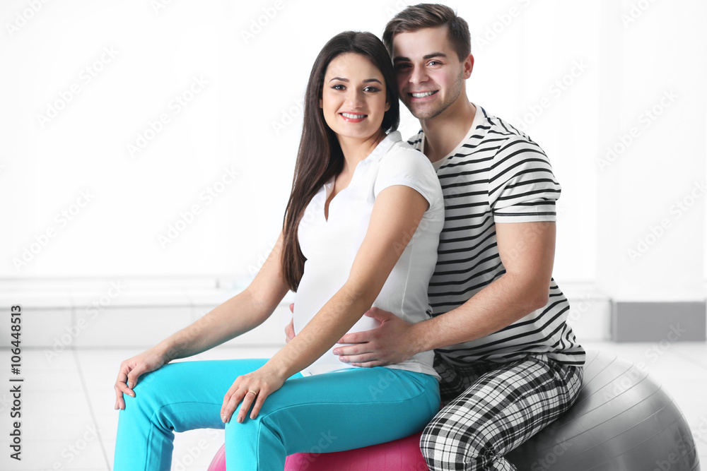 Pregnant woman with husband sitting on a fitness ball in the room Pregnant woman with husband sitting on a fitness ball in the room
