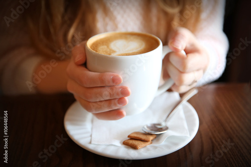 Woman with cup of cappuccino on table in cafe